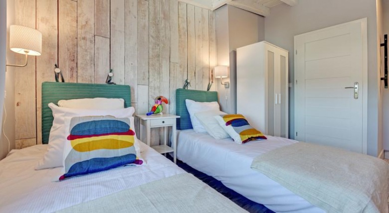 Nad łóżkami w sypialni zawieszono kinkiety, które podkreślają strukturę drewna. Ozdobna ściana świetnie wpisuje się w...