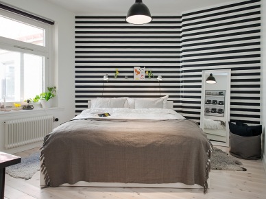 Tapeta w czarno-biale paski,stojące białe lustro i beżowa narzuta na łóżku w sypialni (22980)