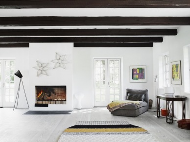 Ciemne drewniane belki na suficie w salonie z kominkiem, szarą leżanką,czarną konsolką i tkanym dywanem w stylu skandybnawskim (26747)