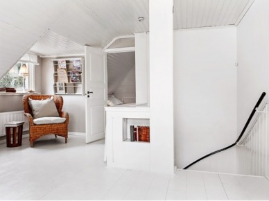 Rattanowy duży fotel z poduszkami,półka na czasopisma na ścianie na białym poddaszu w skandynawskim domku (27875)