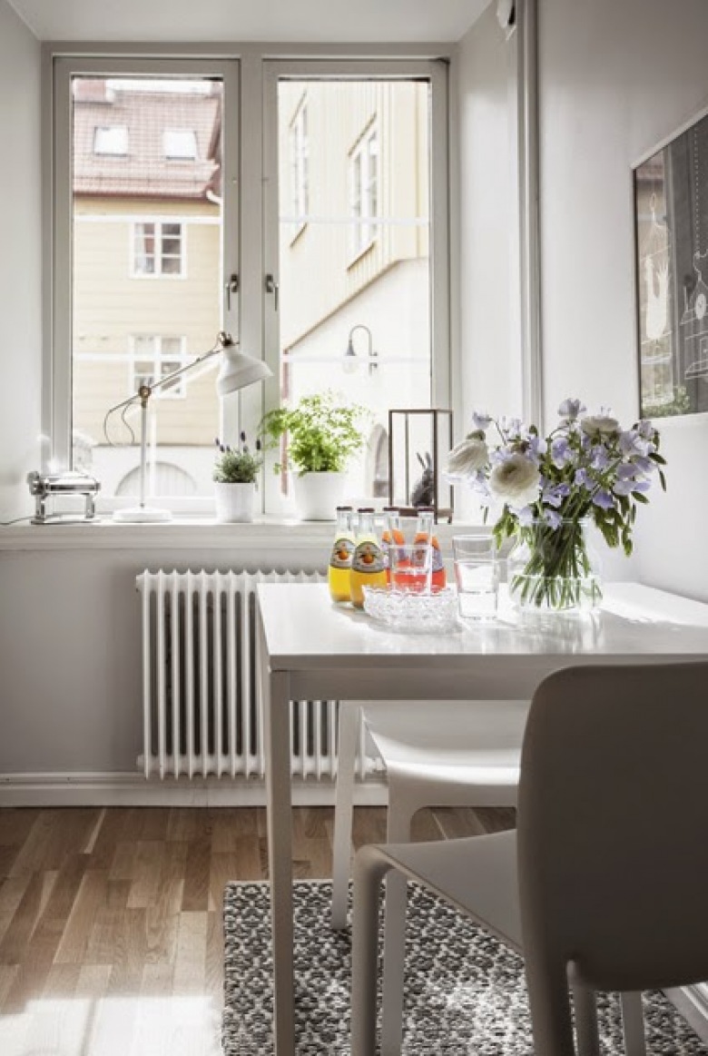 Po prawej stronie pod ścianą w kuchni znajduje się mały stolik z dwoma krzesłami o delikatnej formie. Biały kolor...