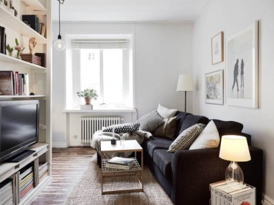 Grafitowa sofa, drewniana postarzana podłoga i biały regała z TV i książkami w małym salonie (24439)
