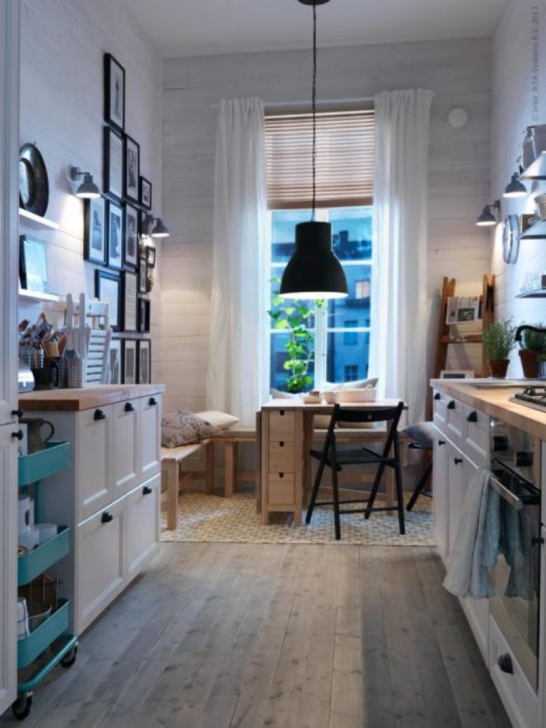 Ikeowska kuchni w bieli z jasną drewnianą podłogą.Jest też galeria na ścianie i czarna lampa nad stołem prze co tworzy...