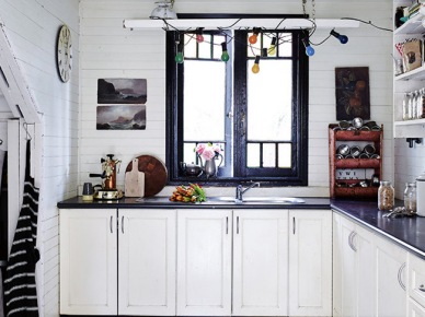 Biala kuchnia z czarnymi blatami i girlandą z kolorowych żarówek przy oknie (24752)