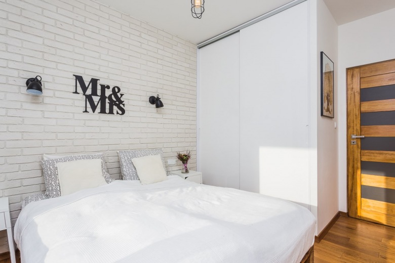 Aranżacja niewielkiej sypialni w stylu skandynawskim. Białe cegły na ścianie dodatkowo eksponują czarną dekorację i...