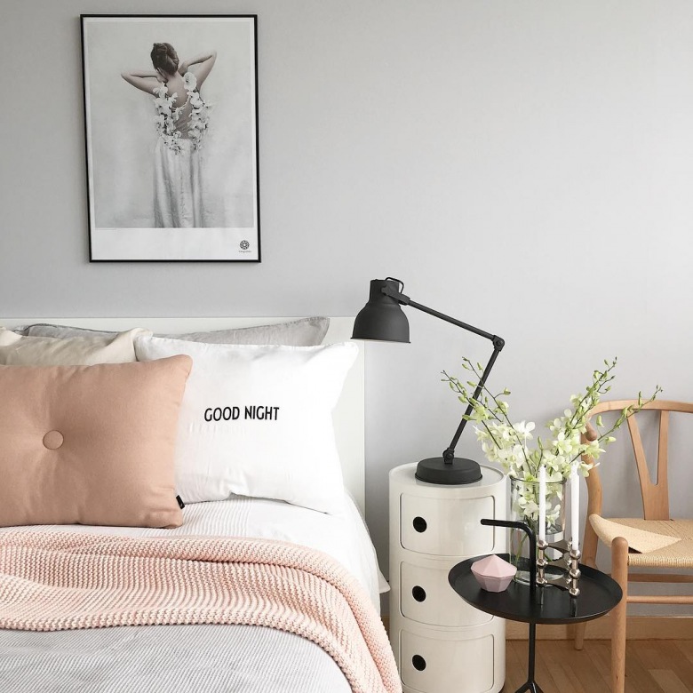 Szarość na ścianie w sypialni stanowi neutralne tło dla dodatków w innych odcieniach. Koc i poduszka w pastelowym różu wnoszą do wnętrza romantyczny...