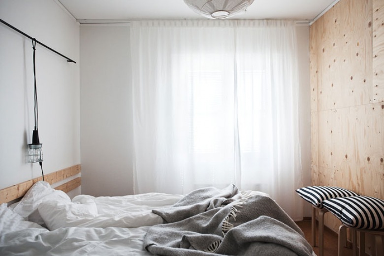 Żarówka w fabrycznej oprawie z amocowana na relingu nad łóżkiem w skandynawskiej sypialni (25445)