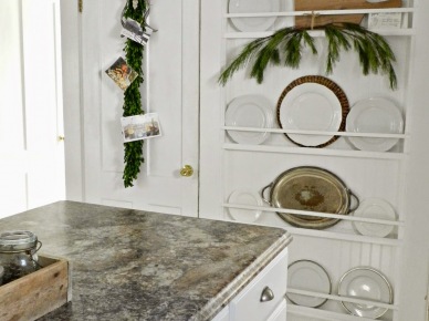 Białe drzwi z zieloną girlandą świąteczną i białe wiszące półki z talerzami na ścianie (27561)