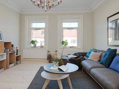 Biało-szary salon z drewnianymi kubikowymi półkami,okragłymi stolikami i szara sofa na drewnianej podstawie (22572)