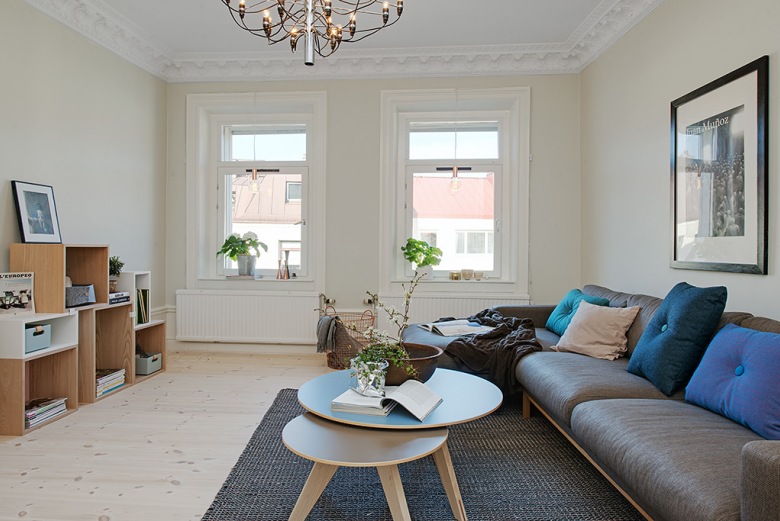 Biało-szary salon z drewnianymi kubikowymi półkami,okragłymi stolikami i szara sofa na drewnianej podstawie (22572)