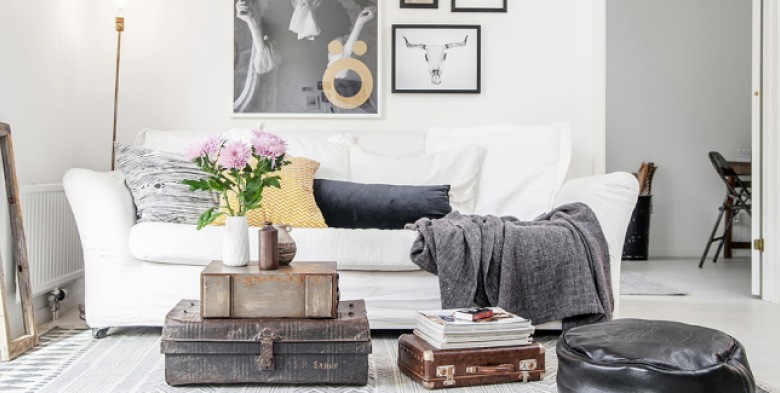 Skórzana i metalowa walizka w stylu vintage,czarna pufa i biała sofa z galerią plakatów na ścianie (24701)