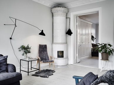 Biały ceramiczny piec w klasyczneym skandynawskim stylu,czarny kinkiet na wysięgniku,bielone deski z drewna na podłodze w salonie (47751)