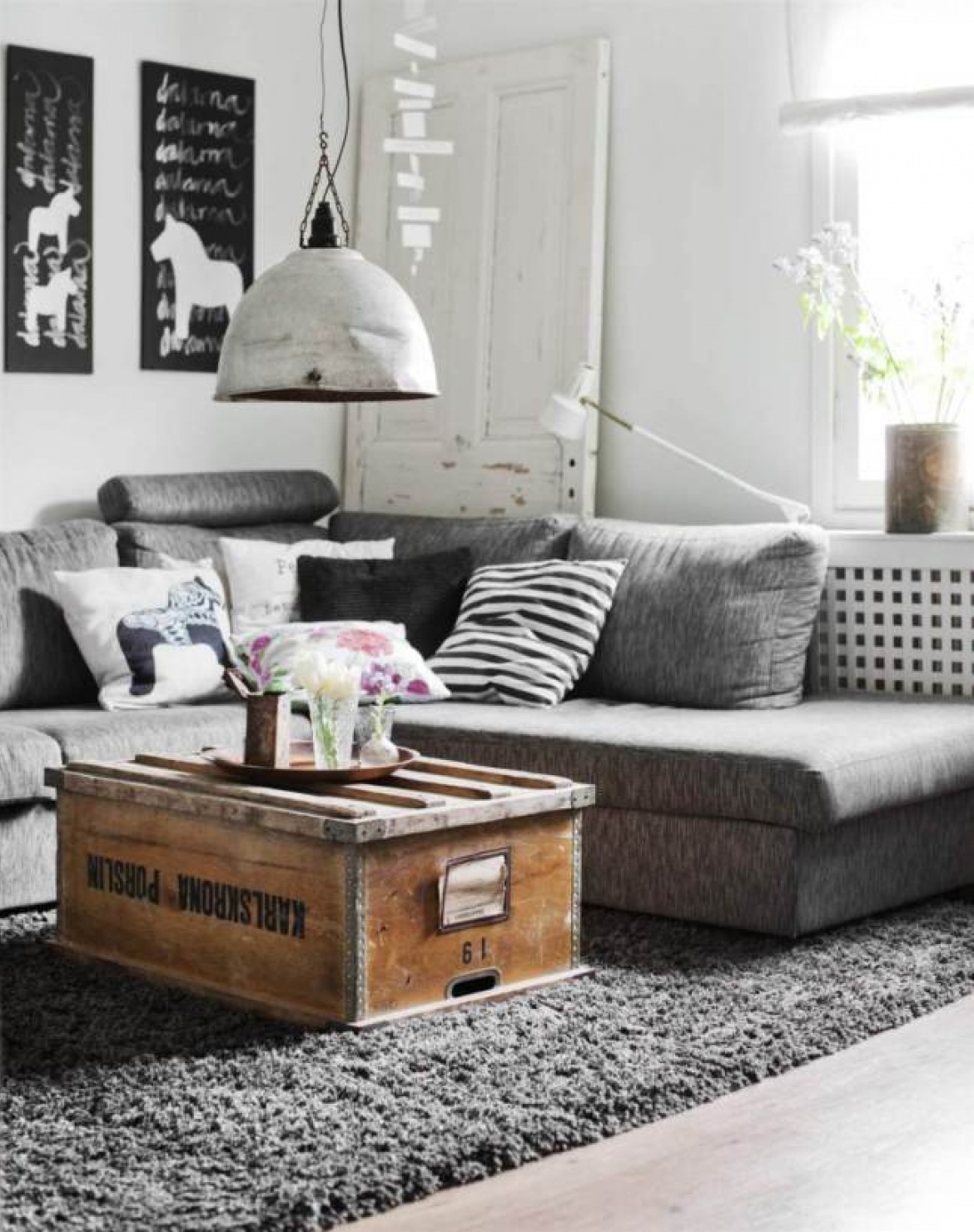 Drewniana skrzynia w roli stolika w aranżacji skandynawskiego salonu z szarą sofą, białą lampa industrialną i biało-czarnymi dekoracjami (28235)