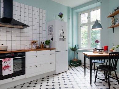 Czarny okap, białe szafki kuchenne z drewnianym blatem,turkusowo-mietowe ściany,biało-czarna terakota na podłodze w kuchni z czarnym stołem i krzesłami (25872)
