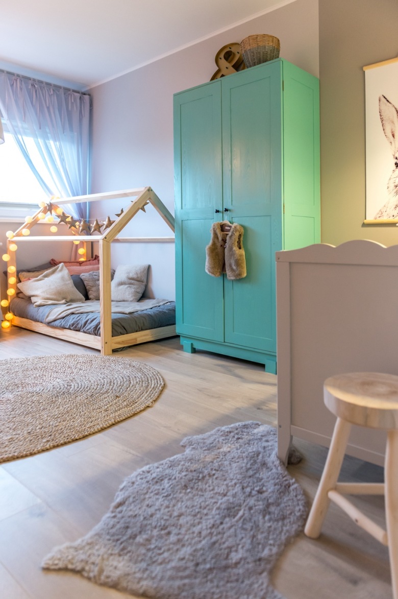 W pokoju dziecięcym znajduje się charakterystyczne łóżko w kształcie domku oraz niebieska szafa do przechowywania...