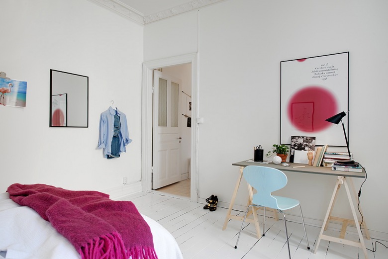 Rózowy pled z frędzlami,plakat z rózowym akcentem i niebieskie krzesło w białej sypialni (24606)