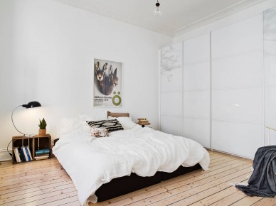 Nowoczesna szafa ze szklanymi drzwiamim przesuwnymi,podłoga z naturalnych desek i drewniane skrzynki w białej sypialni (24725)