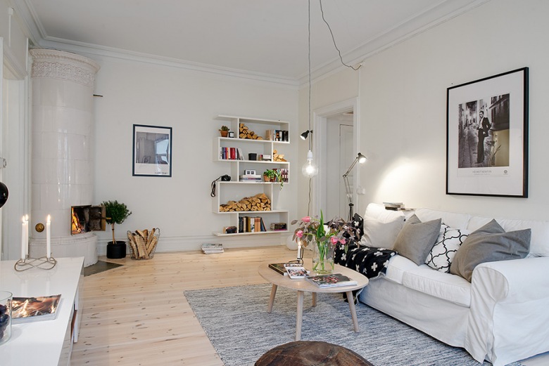 Skandynawski styl w pokoju dziennym - jasna drewniana podłoga, żarówka na kablu w minimalistycznym stylu, biała sofa...