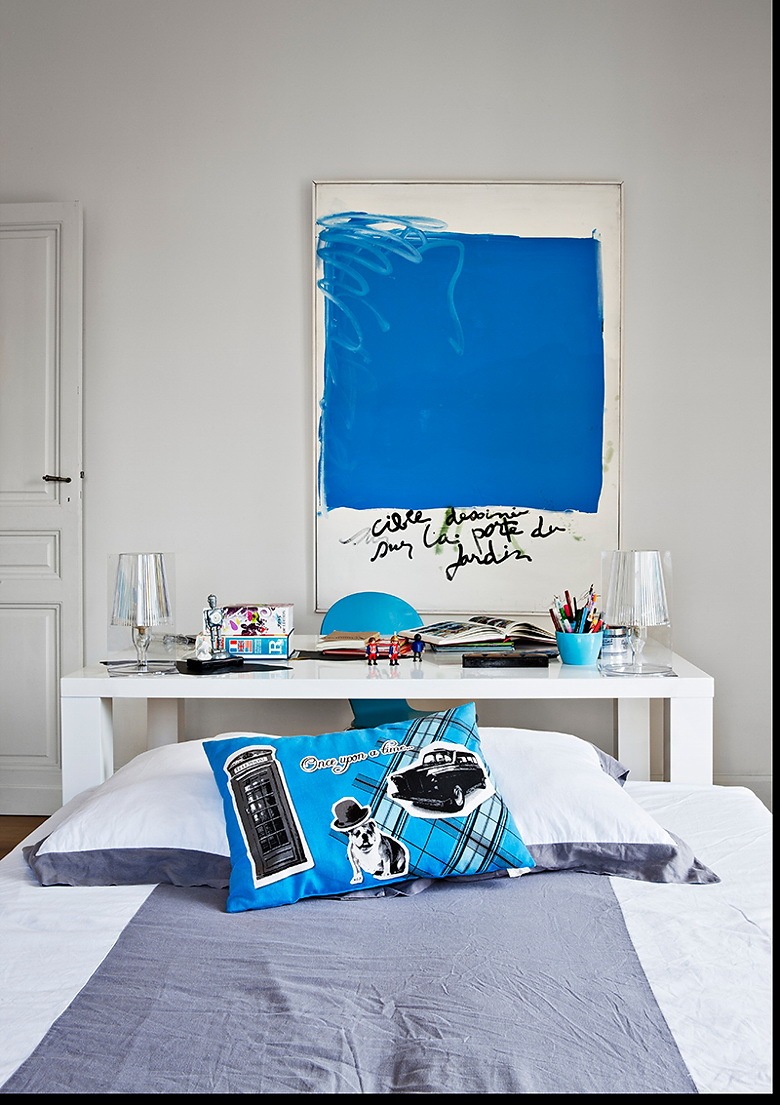 Nowoczesny obraz z niebieskim motywem,niebieska poduszka i detale w białej sypialni z biurkiem (25398)