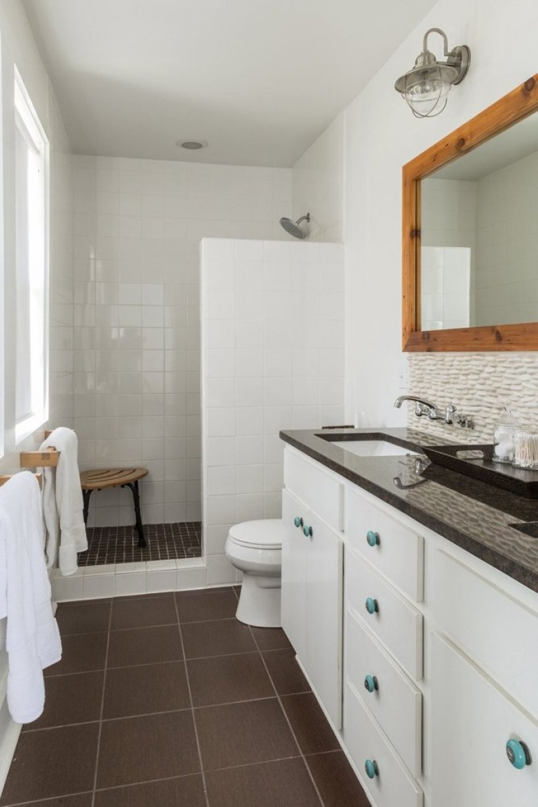 Higienicznie biała łazienka ocieplona drewnianą ramą lustra i brązową podłogą oraz blatem w takim samym kolorze. Duża...