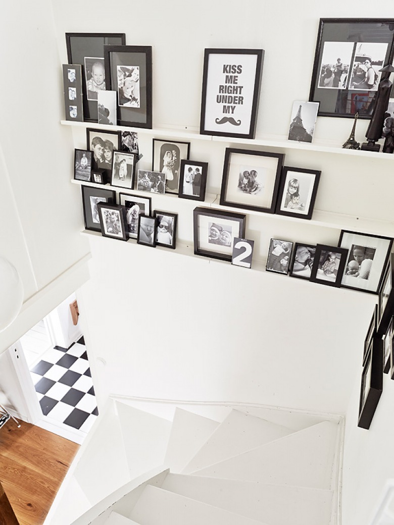 Białe zawijane schody i świetnie przystrojona ściana z fotografiami i obrazami.
