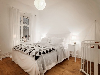 Biało-szaro-czarne trójkaty na skandynawskiej narzucie w białej sypialni małżeńskiej z drewnianym dziecięcym łóżeczkiem (27100)