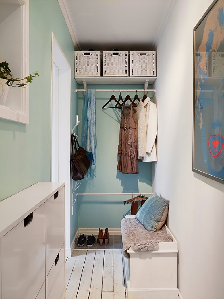 Niebiesko-turkusowa ściana,biale kosze pojemniki z wikliny,wąska szafka wisząca na buty,biała szafka skrzyniowa na podlodze i kolorowy nowoczesny plakat na ścianie (25823)
