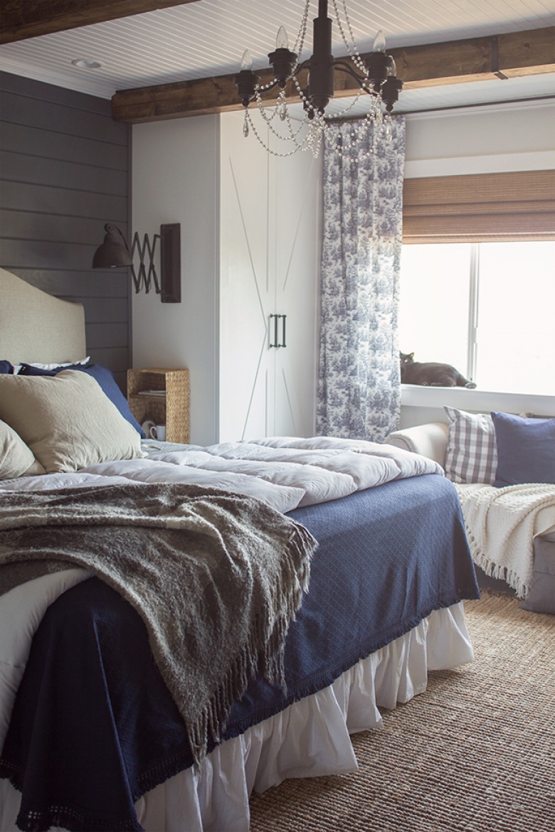 Niebieska narzuta do bezowego łóżka to idealna kombinacja w sypialni. Ściana z drewna w szarym kolorze , biała szafa i...