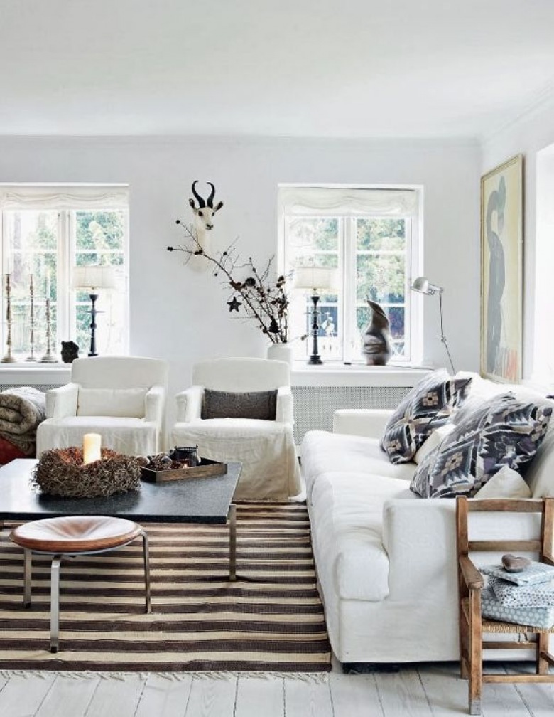 Białe sofy w salonie,drewniane fotele,biało-brązowy dywan w pasy i małe stoliki kawowe i monochromatyczne kolory poduszek dekoracyjnych (27413)