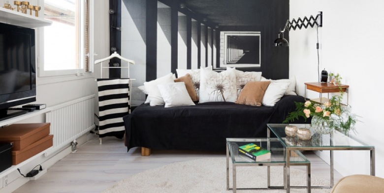 Czarna sofa z białymi i jasno-brązowymi poduszkami na tle ściany z fototapetą,metalowe kwadratowe stoliki ze szkłem i jasna podłoga z drewna w salonie (26261)
