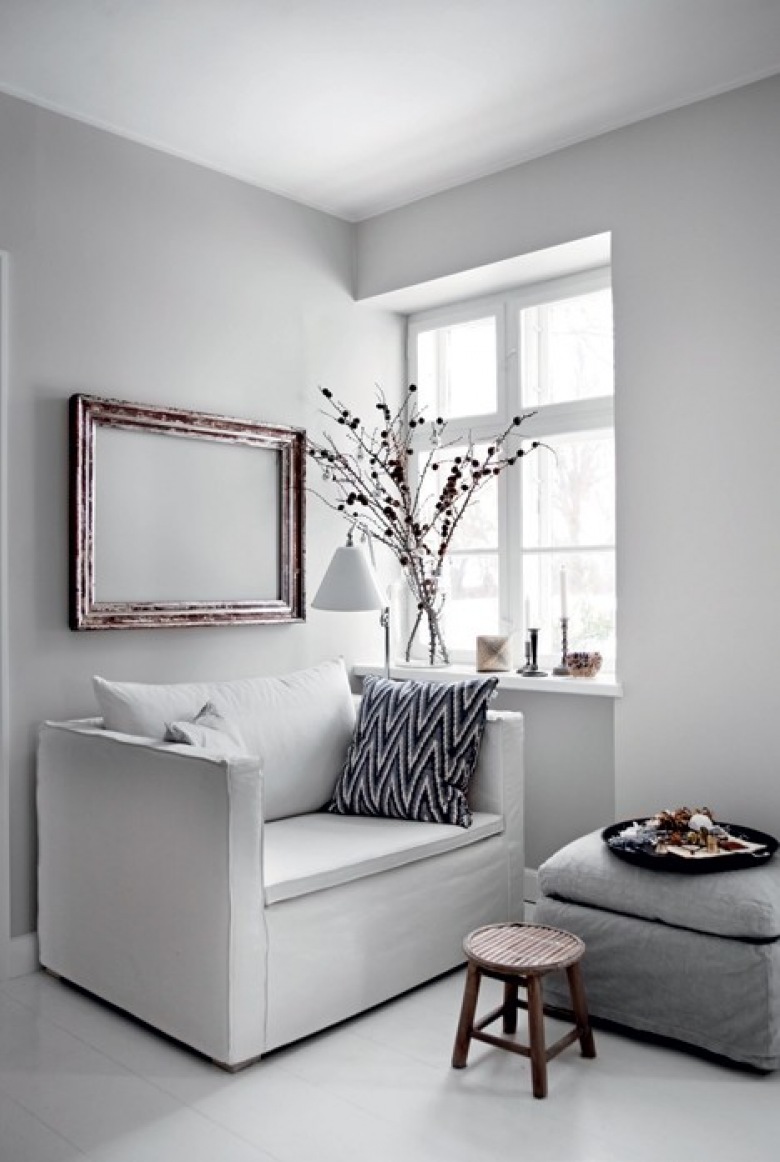 Minimalistyczna biała sofa z szarym podnóżkiem,drewniane ramy vintage i drewniany taboret w salonie przy oknie (27406)