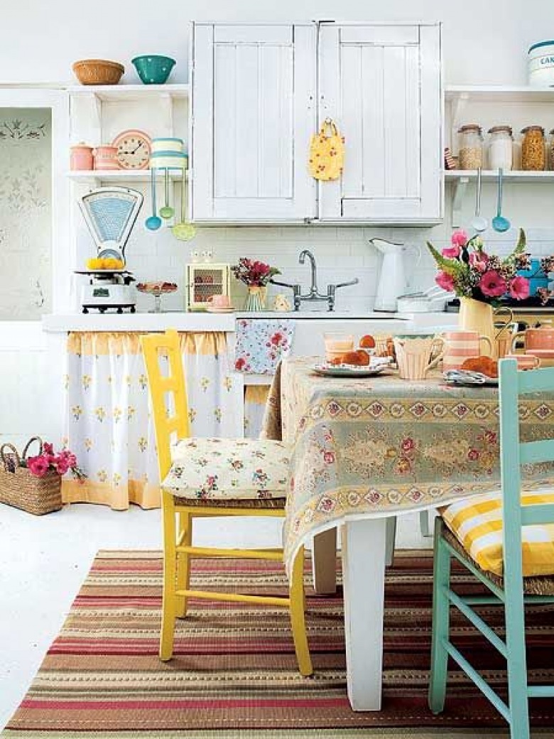 Wiejska kuchnia z żółtymi i turkusowymi krzesłami,tkanymi kolorowymi dywanikami w paski,kwiecistym obrusem i dodatkami z emaliowanej blachy (26603)