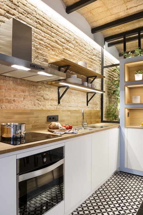 W aranżacji kuchni skupiono się na połączeniu piaskowych cegieł na ścianie z drewnianymi deskami na suficie. Dla...