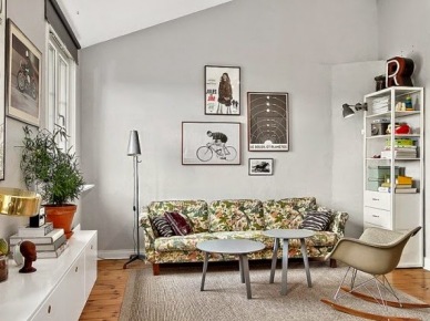 Szare okrągłe stoliki kawowe,fotel na płozach,kwiecista sofa i oryginalne grafiki na szarych ścianach w salonie (26381)