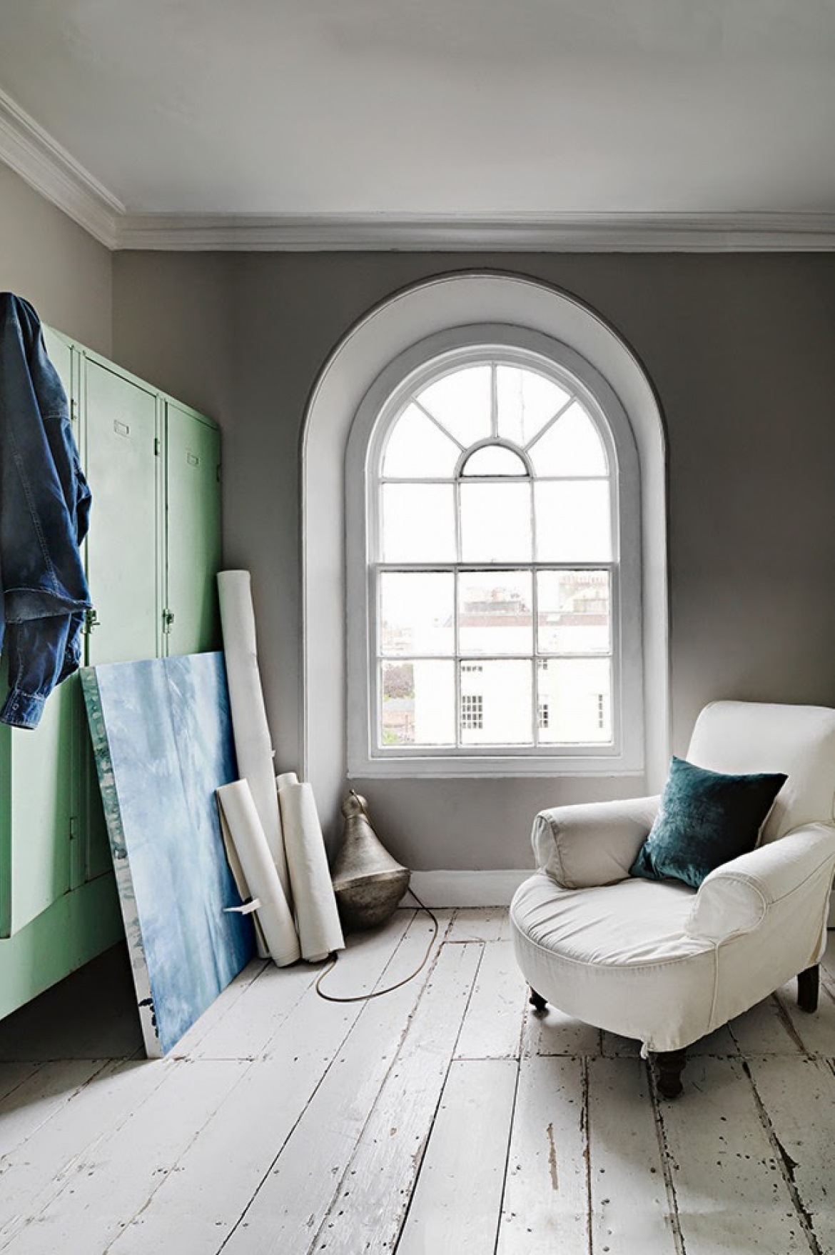 Szare ściany,turkusowa metalowa szafa,biały fotel na kółkach i okno z łukiem (25063)