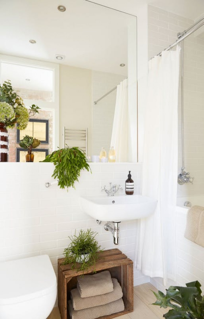 W łazience króluje biel i naturalne elementy. Skrzynka z drewna odgrywająca rolę szafki oraz zielone doniczkowe kwiaty...
