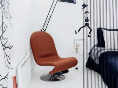 Karmelowy nowoczesny fotel na chromoniklowanej podstawie,czarna lampa podłogowa,białe ściany i czarne łóżko (47693)