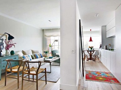 Otwarta przestrzeń mieszkania z widokiem na biała kuchnię i turkusowe detale w salonie (20447)