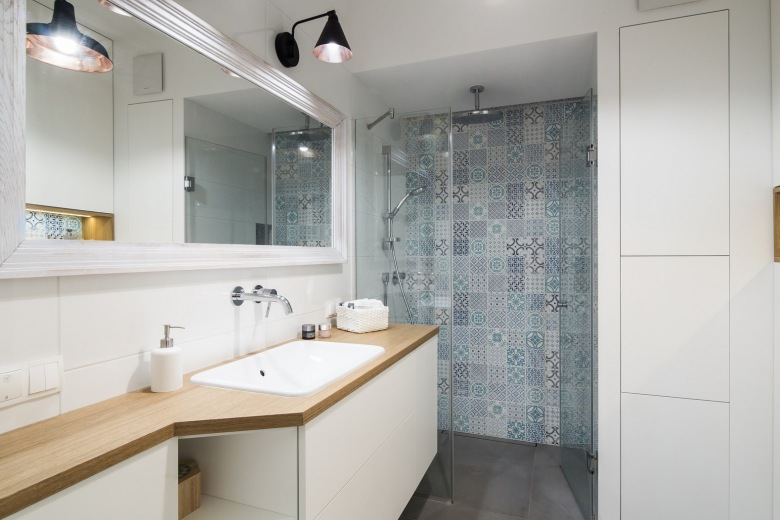 Aranżacja całkiem przestronnej łazienki w stylu skandynawskim, gdzie dominuje biel i drewno. Wzorzysta ściana w części prysznicowej urozmaica cały wystrój. Wprowadza oryginalny klimat, przełamując stonowane...