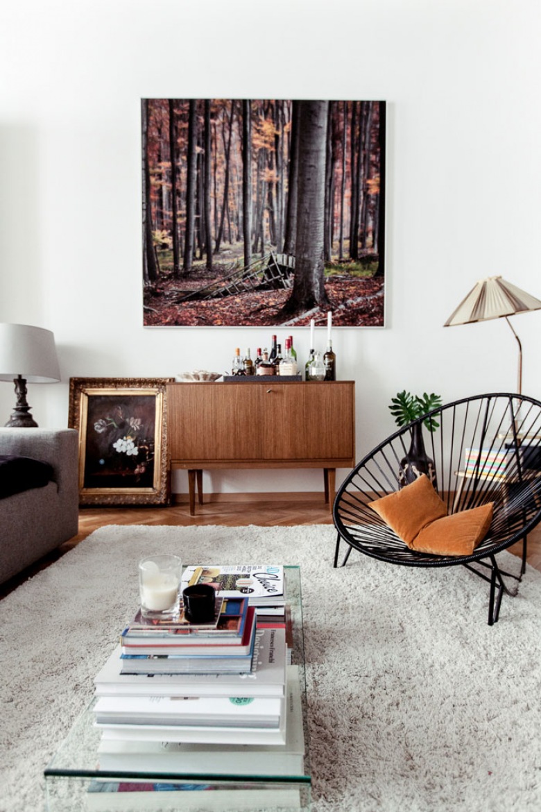 Biały futrzany dywan,ażurowy okragły fotel,obrazy i brązowa komoda z lat 60-tych w białym salonie w stylu eklektycznym (25577)