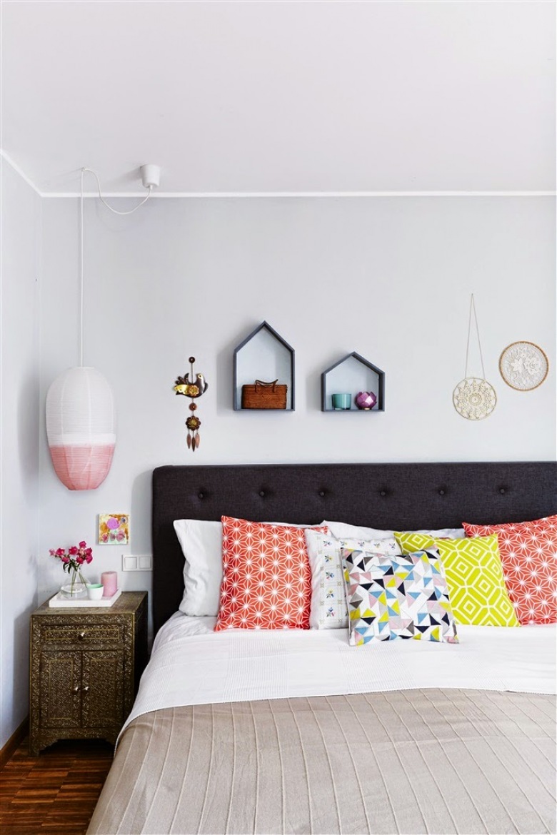 Ciemne meble stanowią mocny kontrast z jasnymi ścianami. Wzorzyste poduszki w kolorze, podobnie jak dodatki o geometrycznych kształtach (lampa wisząca czy półki na ścianie) wypełniają przestrzeń, ozdabiając...