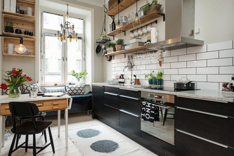 Biało-czarną przestrzeń w kuchni urozmaicają elementy z drewna, takie jak otwarte półki czy szuflady w stoliku...