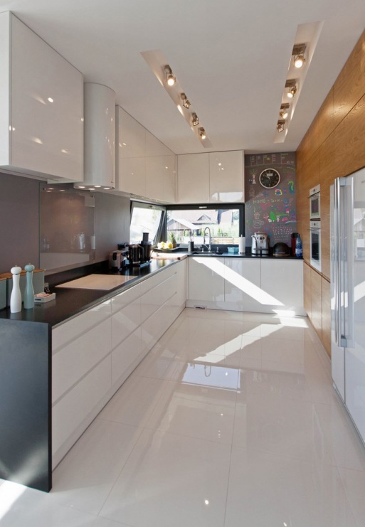 Białe szafki z połyskiem podkreślają nowoczesny stylu kuchni. Farba tablicowa na ścianie w głębi pomieszczenia dekoruje...