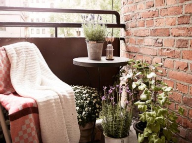 Mały balkon z fotelem,okrągłym stolikiem,roslinami w doniczkach i czerwoną cegłą na ścianie (25987)