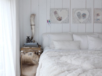 Dekoracyjne serca w białej sypialni z futrzaną narzutą, drewnianą podłogą i szafką kufrem w beżowo-białym futerku (27682)