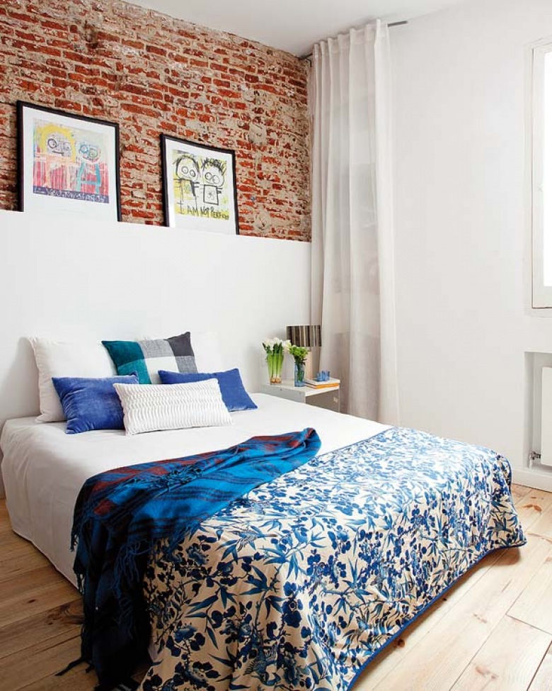 Niebieska narzuta na łóżko z czerwoną cegłą na ścianie idealnie wpisuje się w charakter nowoczesnej,ale jakże...