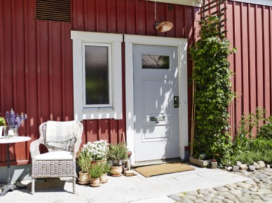 Czerwona elewacja skandynawskiego domu z szarymi drzwiami i małym ogródkiem przed domem (24668)