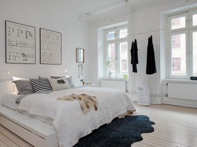 Biała sypialnia skandynawska z typografiami na ścianie i szarym futrzakiem na drewnianej podłodze (22590)