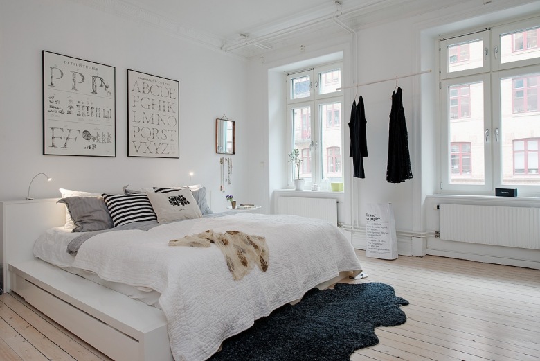 Biała sypialnia skandynawska z typografiami na ścianie i szarym futrzakiem na drewnianej podłodze (22590)