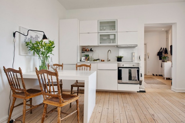 Biala kuchnia w nowoczesnymstylu, gdzie drewniane krzesla i podloga dodaja jej skandynawskiego charakteru.